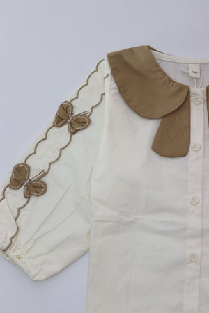 Baby romper with beige trim and buttons on a light gray background